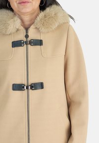 Abrigo de lana beige con cuello de piel sintética, cremallera plateada y cierres de toggles negros. Textura suave con un diseño estructurado.