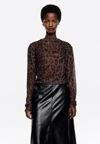 Długi rękaw brązowy top z siateczki w czarne leopardzie wzory, połączony z czarną błyszczącą skórzaną spódnicą. Teksturowany materiał z dopasowanym krojem.