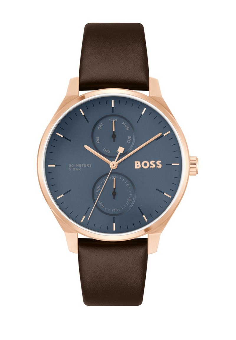 Montre ronde avec un cadran bleu foncé, aiguilles et logo en or rose, deux cadrans plus petits pour le jour et l'heure, bracelet en cuir marron et boîtier en acier inoxydable.