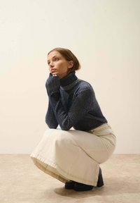 Dunkelblaues, geripptes Turtleneck-Pullover mit langen Ärmeln, kombiniert mit einem cremfarbenen, fließenden Midikleid und klobigen schwarzen Plateaustiefeln.