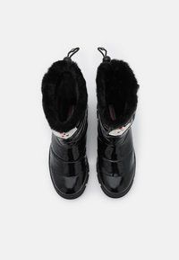 Bottes de pluie en vernis noir avec doublure en fourrure douce noire, tige haute et anses. Bout rond et semelle en caoutchouc texturé pour une meilleure adhérence.