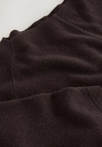 Black wool sweater with ribbed cuffs, featuring a soft texture and smooth surface, showing slight folds and natural fibers.