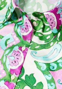 Blouse colorée à motif floral mêlant rose, vert et turquoise, avec un col classique et des boutons nacrés sur la patte de boutonnage.