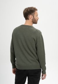 Olijfgroene trui in een ribbelbrei, met een ronde hals, lange mouwen en een relaxte pasvorm. Zachte textuur met een subtiele glans.