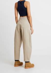 Béžové kalhoty s širokým střihem a zadními kapsami, kombinované s přiléhavým námořnickým crop topem a hnědými šněrovacími botami s robustní podrážkou.