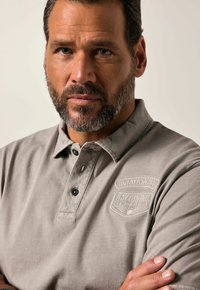 Šedé polo tričko s límečkem, čtyřbuttonovou légou a texturovanou látkou. Obsahuje vyšitý logo na hrudi.
