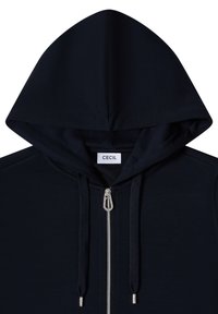 Sweat à capuche zippé bleu marine avec cordons de serrage et une fermeture éclair argentée, avec une étiquette blanche "CECIL" à l'intérieur du col.