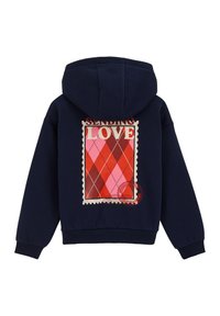 Tumši zila kapuce ar drukātu pastmarkas dizainu, uz kura ir vārdi "SŪTĪTU MĒLESTĪBU", iekļaujot dimanta rakstu sarkanos un rozā toņos.