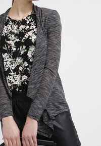 Gray knit cardigan with draped front, paired with a black floral blouse. Blouse features pink and white flowers on a black background.