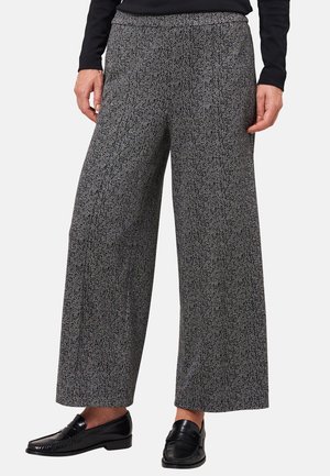 Graue Hosen mit weitem Bein und dezentem Fischgrätmuster, kombiniert mit schwarzem Langarmshirt und schwarzen Leder-Loafern.