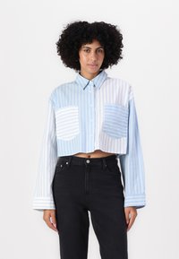 Blå och vit randig kortärmad skjorta med knäppning framtill, med två framfickor och långa ärmar. Svarta högmidjade jeans.