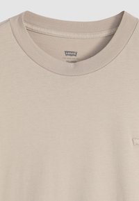 Beige Baumwoll-T-Shirt mit einem Rundhalsausschnitt, geripptem Kragen und einem kleinen gestickten Logo auf der Vorderseite. Glatte Textur, lockere Passform.