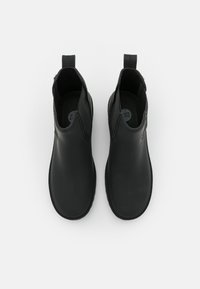 Botines negros de tipo ankle hechos de caucho con un acabado suave. Presentan tiradores para facilitar el uso y un diseño flexible con un minimalismo en los detalles.