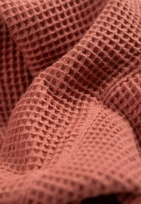 Gestructureerde terracotta stof met een wafelweefpatroon, die een zachte, dichte textuur en subtiele glans toont.