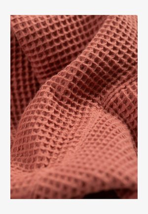 Tissu en terracotta texturé avec un motif en relief en nid d'abeille, mettant en valeur une texture douce et dense ainsi qu'un éclat subtil.