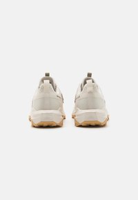 Zapatillas deportivas de color gris claro con parte superior texturizada, lengüetas de tiro y suelas de goma resistentes con clavos de tracción multidireccional.