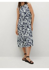 Robe sans manches en navy avec un motif floral blanc, longue jusqu'aux genoux, coupe ample, taille froncée. Associée à des sandales noires à lanières.