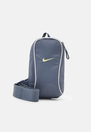 Kompaktowa granatowa torba na ramię Nike z żółtym logo Swoosh, zamkiem błyskawicznym i regulowanym paskiem na białym tle.