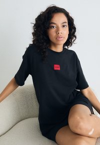 Juoda per didelis t-shirt su trumpomis rankovėmis, turintis raudoną stačiakampio formos "HUGO" logotipą ant krūtinės. Minkšta medžiaga ir laisvas siluetas.