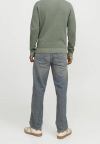 Grön texturerad tröja med ribbade muddar och nederkant, i kombination med ljusblå jeans. Skorna har beige och krämfärgade accenter på en gummisula.