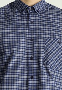 Camicia a quadri con tonalità blu, navy e bianco. Collo button-down, chiusura frontale con bottoni e taschino sul petto con motivo abbinato.