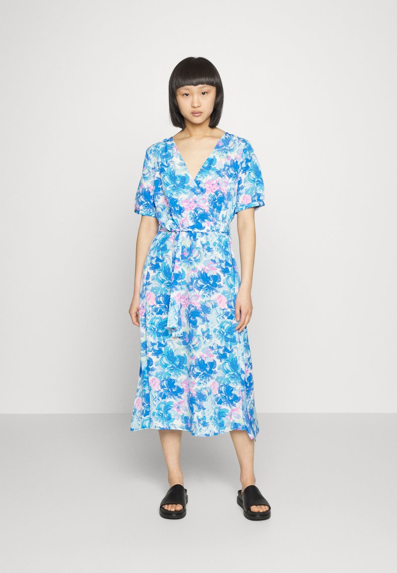 Vestido de flores em azul, rosa e branco. Mangas curtas bufantes, decote em V e detalhe de laço na cintura. Tecido suave com uma silhueta fluida.