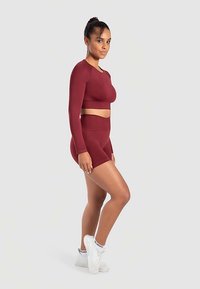 Vinrött träningsset med långärmad croptop och högmidjade shorts. Slät textur, figurnära design, kombinerat med vita sneakers.