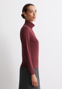 Burgunderfärgad långärmad polotröja tillverkad av mjukt, stretchigt tyg. Har en åtsittande design och en hög krage.
