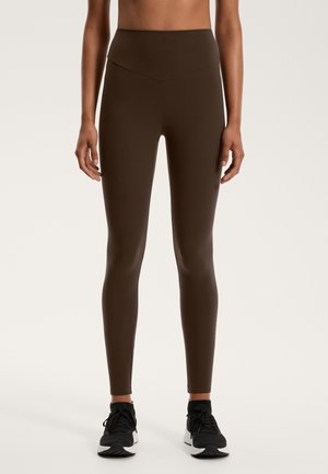 Barna, magas derekú leggings, amelyek áramvonalas szabással készültek, rugalmas anyagból. Fekete sportcipővel párosítva teljes a megjelenés.