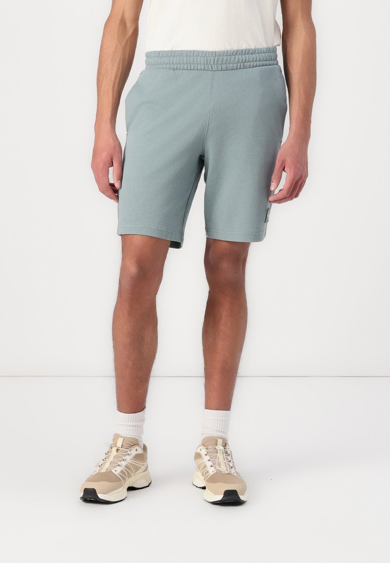 Șorturi atletice de culoare albastră deschisă, cu un tiv elastic și buzunare laterale. Asortați cu sneakers bej și șosete albe până la glezne.