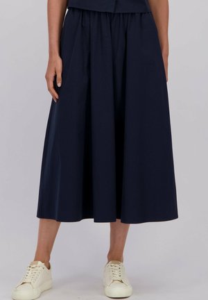 Marine midi-rok gemaakt van solide stof met een geplooid tailleband, met een vloeiende silhouet en gecombineerd met witte sneakers.