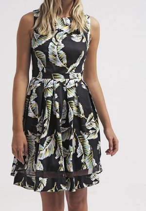 Czarna sukienka bez rękawów z wielokolorowym wzorem z piór i dopasowaną talią, noszona przez stojącą osobę na jednolitym tle.