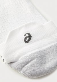 Weiße und graue Baumwollsocke mit strukturiertem Strickbund und schwarzem, kleingeschriebenem "a", das nahe der oberen Kante gestickt ist.