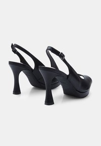 Crne cipele sa visokom potpeticom i otvorenom petom, s okruglim vrhom, glatkom kožnom teksturom i okruglim izrezom. Imaju dekorativnu kopču.
