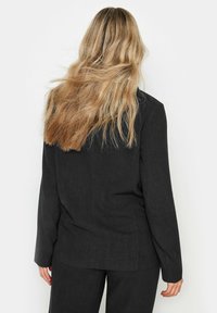 Mustat bleiserit, joissa on rento leikkaus, pitkät hihat, sileä pinta ja minimalistinen muotoilu, jossa on puhtaat linjat ja ei näkyvää metalliosaa.