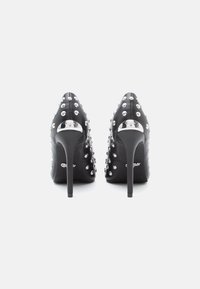 Svarte høyh�ælte sko med spisse tær, dekorert med sølvnitter, med en metallisk aksent på hælen og en glatt tekstur.