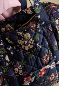 Granatowa pikowana torba typu tote z wielobarwnym kwiatowym wzorem, złotym zamkiem błyskawicznym i czarną metką "JOULES". Tkanina o fakturze z miękkim wykończeniem.