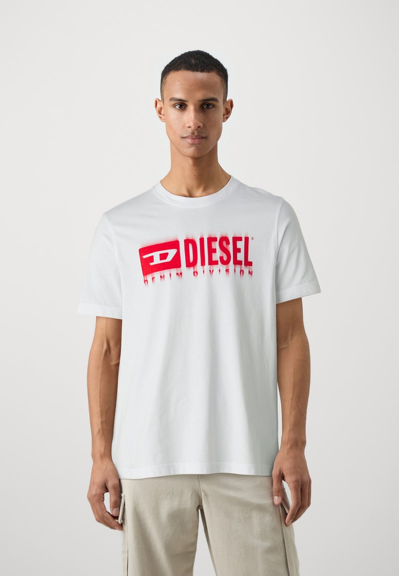 T-shirt en coton blanc avec un logo rouge "DIESEL" et le texte "DENIM DIVISION". Manches courtes, encolure ras du cou, coupe décontractée.