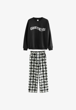 Czarny sweatshirt z napisem "GHOSTING YOU"; połączony z luźnymi czarno-białymi spodniami dresowymi w kratę z wzorem duchów.