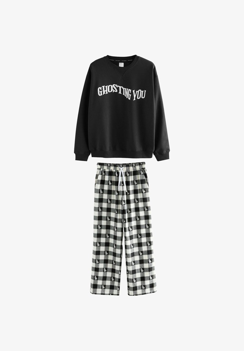Sweatshirt noir avec le texte « GHOSTING YOU » ; associé à un pantalon de pyjama large à carreaux noirs et blancs avec des motifs de fantômes.