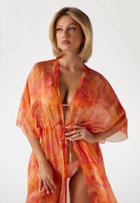 Kimono trasparente in vivaci tonalità di arancione e rosa con vita legata. Presenta un tessuto leggero e maniche ampie, creando una silhouette fluida.