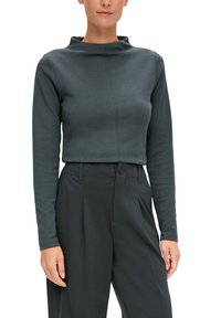 Top a maniche lunghe grigio scuro con collo alto e design aderente; presenta linee pulite e una texture morbida. Abbinato a pantaloni neri su misura.