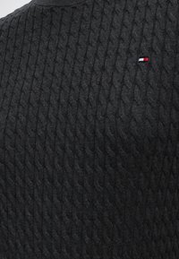 Tissu en maille torsadée gris foncé avec un petit logo rectangulaire rouge, blanc et bleu en haut à droite.
