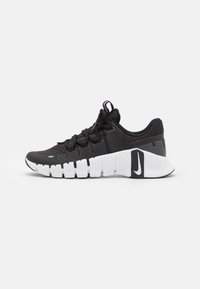 Sort atletisk sneakersko med en tekstureret overdel, hvid segmenteret sål og sorte detaljer, med runde snørebånd og en løftestrop ved hælen.