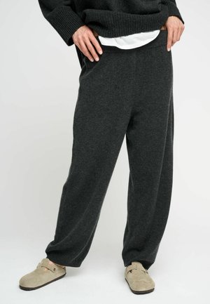 Pantaloni grigi scuri, larghi e comodi, realizzati in tessuto morbido con una vita ampia. Abbinati a scarpe beige senza lacci per il massimo del comfort.