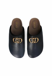 Zwarte leren instapmules met een ronde gouden hardware-logo accent. Zachte bruine binnenzool met merknaam in reliëf. Gladde textuur.