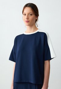 Navyblauw T-shirt met korte mouwen en witte accenten op de schouders. Gemaakt van zacht materiaal, met een comfortabele pasvorm en een ronde hals.
