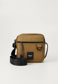 Pruun lõuendist risti kandmisega kott, millel on tõmblukk, reguleeritav rihm, metallist detailid ja bränditud tähis. Kompaktne, ruudukujuline disain tekstuurse pinnaga.