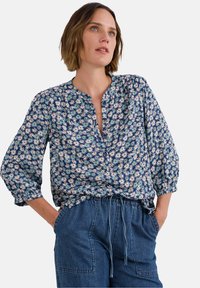 Blouse florale avec fond bleu marine, ornée de petits motifs blancs, jaunes et rouges, dotée d'un décolleté en V et de manches bouffantes.