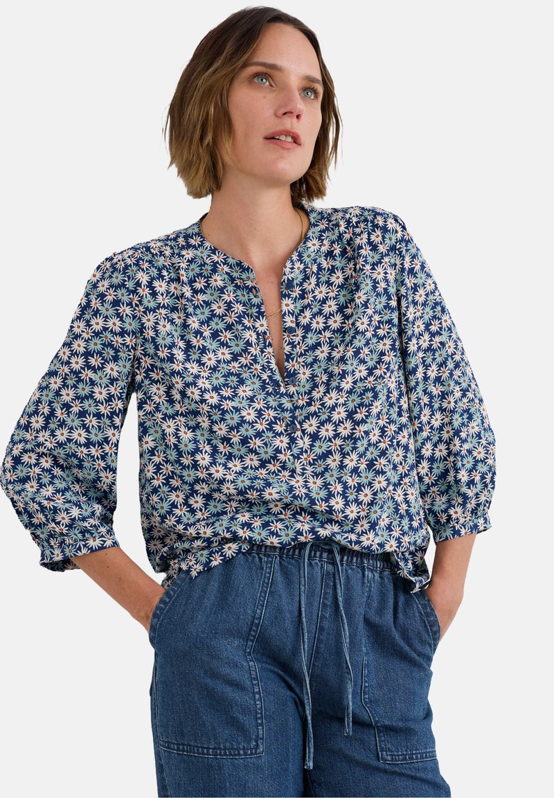 Blouse florale avec fond bleu marine, ornée de petits motifs blancs, jaunes et rouges, dotée d'un décolleté en V et de manches bouffantes.